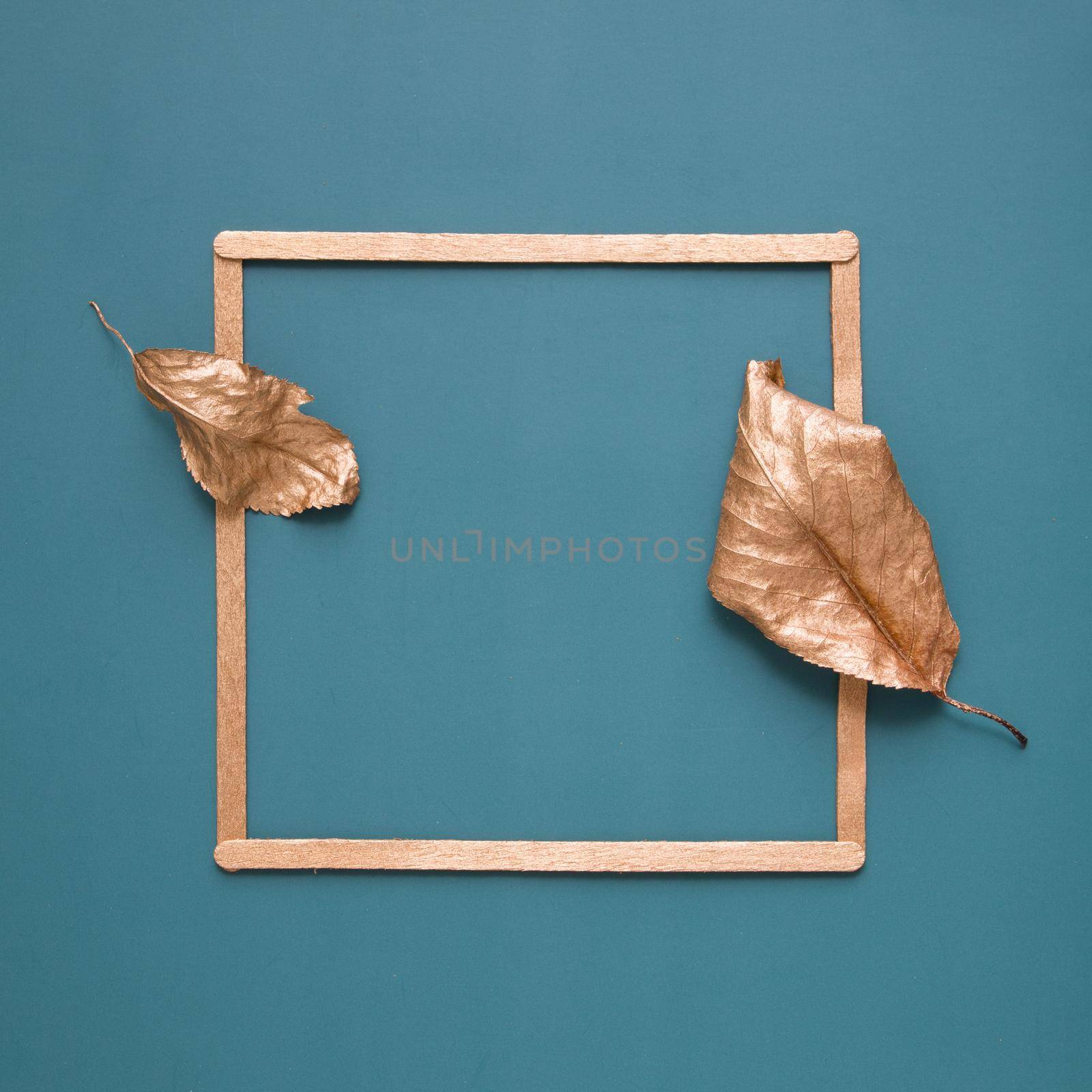 Flat lay of gold leaves and a frame on a turquoise background with copy space by ssvimaliss