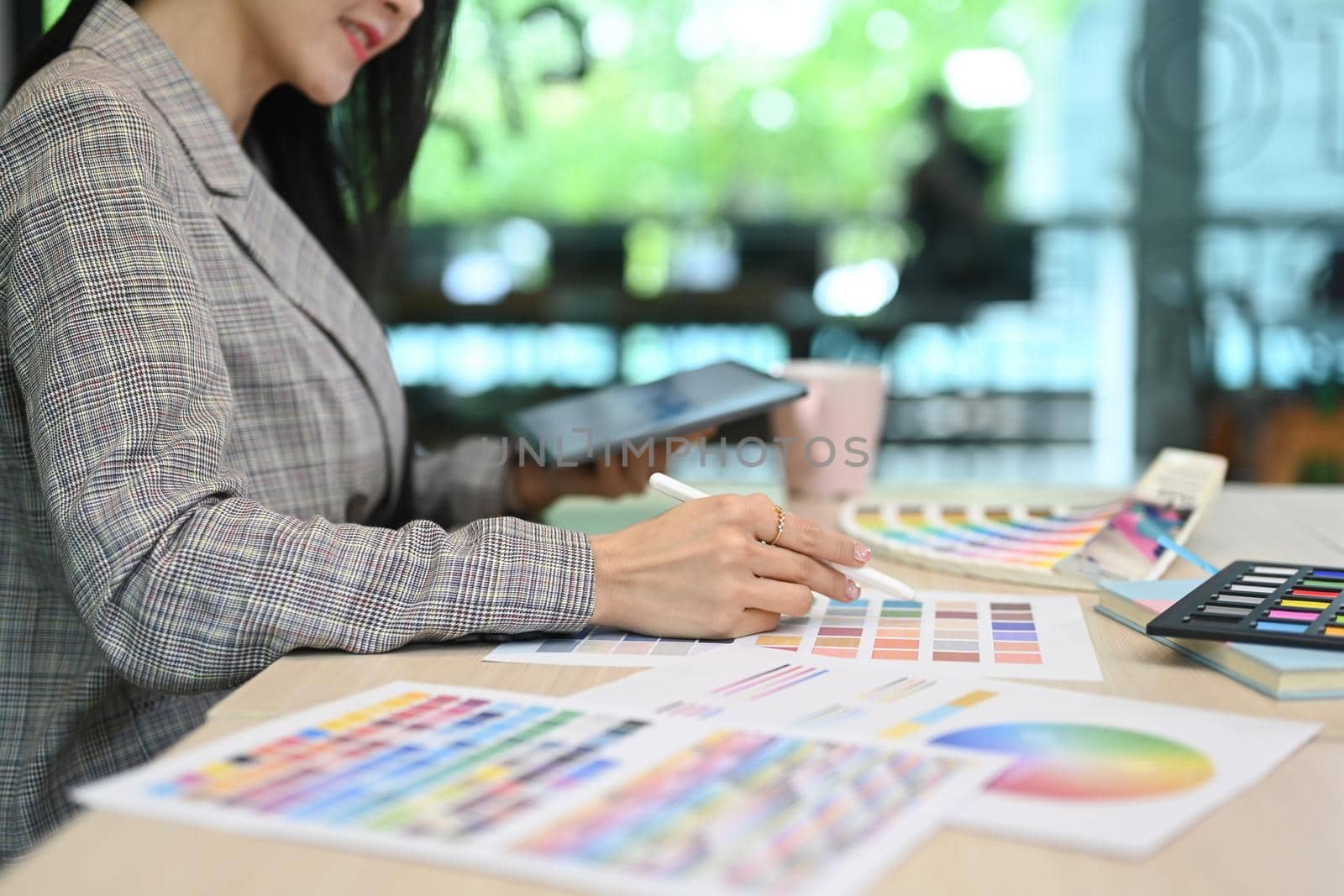 Cropped view of female interior designer using digital tablet and working with color swatches at workplace by prathanchorruangsak
