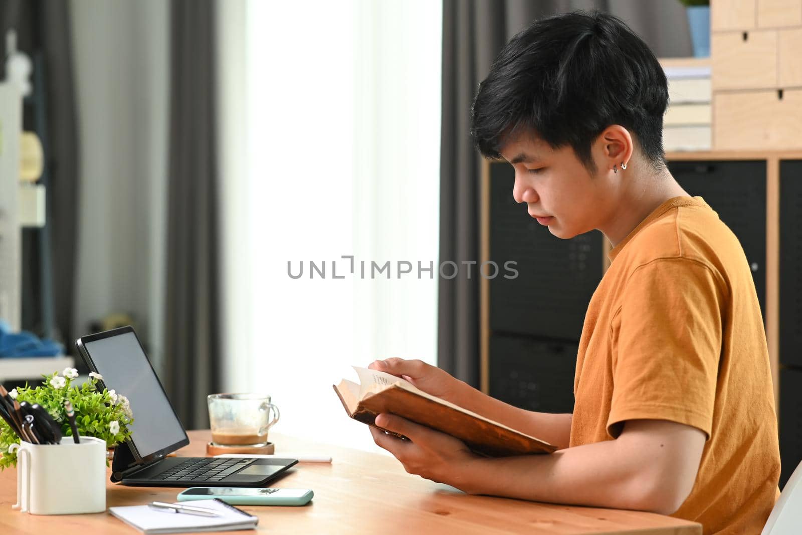 Young man in casual clothes reading book in living room.