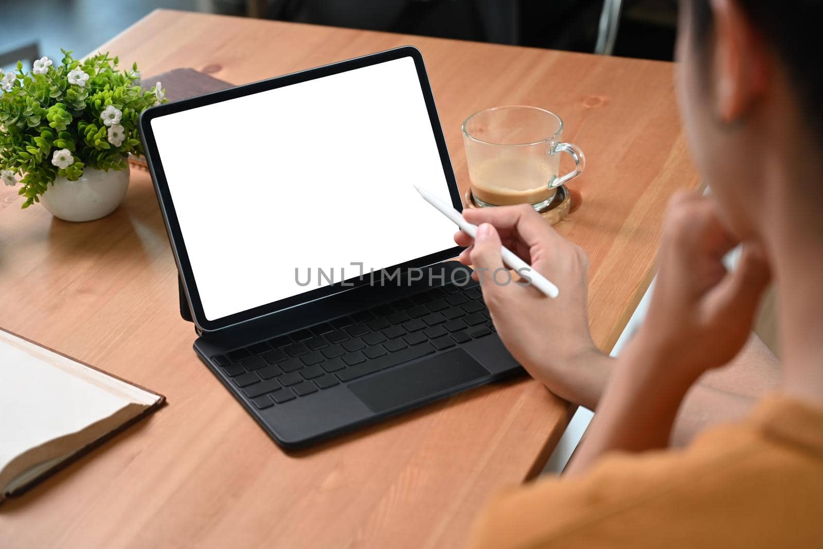 View over shoulder young man using computer tablet on wooden desk. by prathanchorruangsak