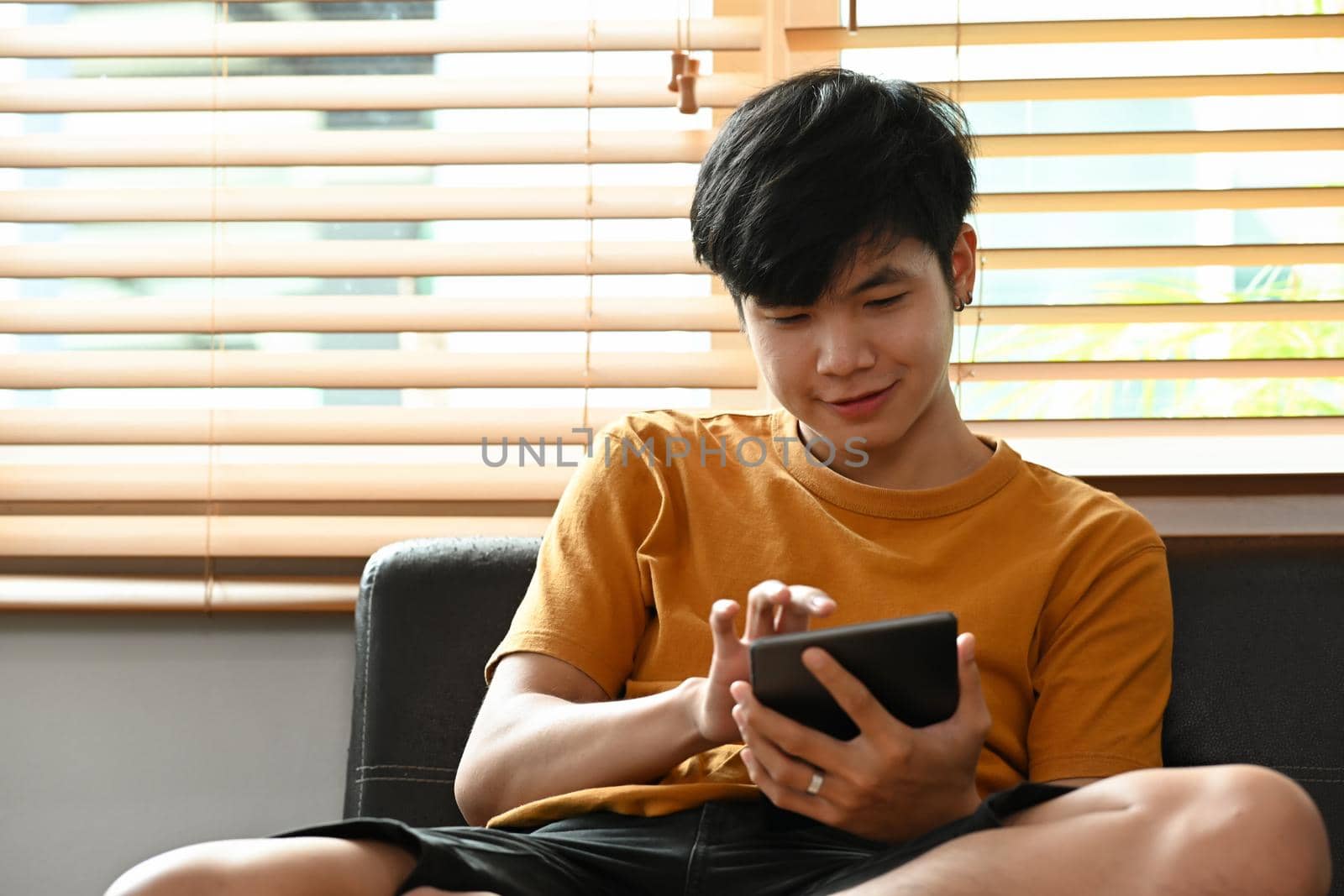 Smiling casual man sitting on couch and using digital tablet.