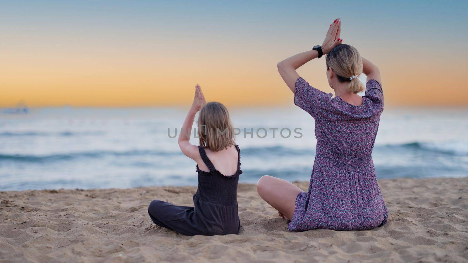 Mother and daughter do yoga on beach in evening. People have fun outdoors. Concept of summer holidays and friendly family and relaxation.