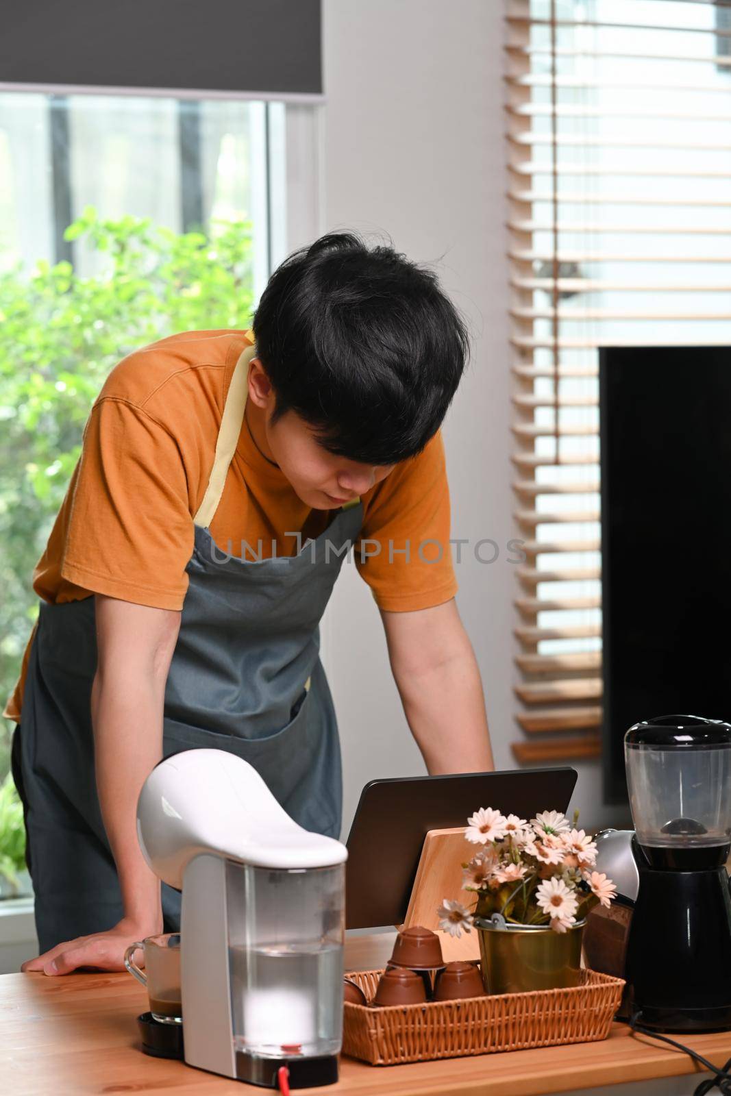 Young man using computer tablet and making coffee with a coffee machine. by prathanchorruangsak