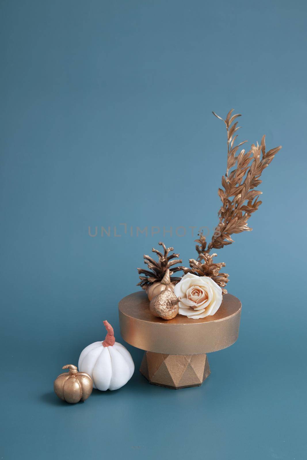 Creative still life of gold and white pumpkins, acorns and rose on a turquoise background. Minimalistic autumn concept.
