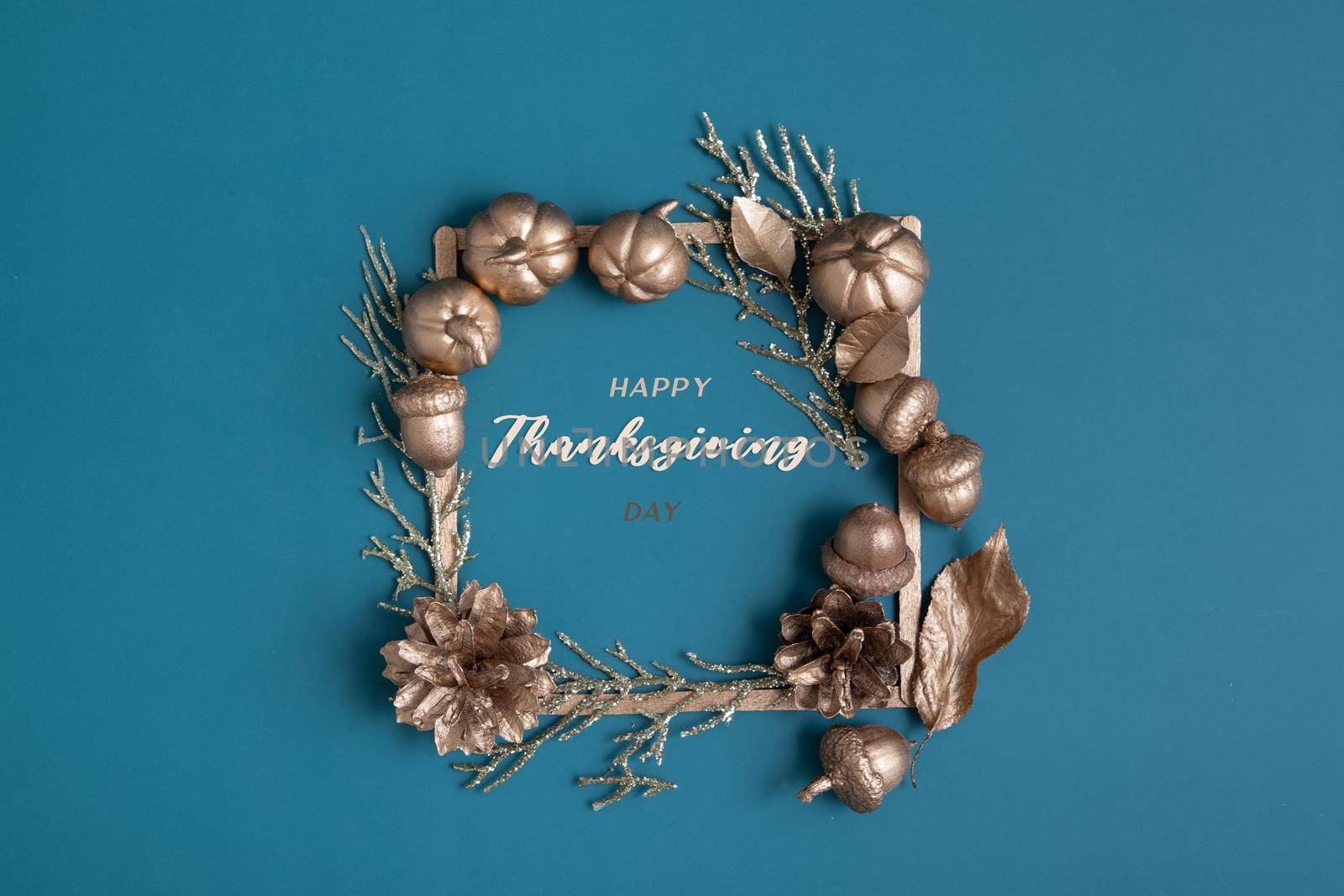 Happy Thanksgiving lettering with flat lay golden pumpkins and acorns on a turquoise background. Creative greeting