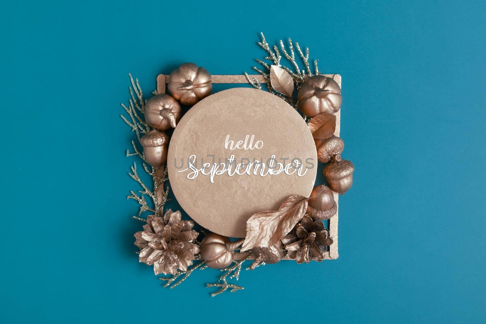 Hello september text and still life of golden acorns, cones, leaves and pumpkins on a turquoise background with a pedestal. High quality photo