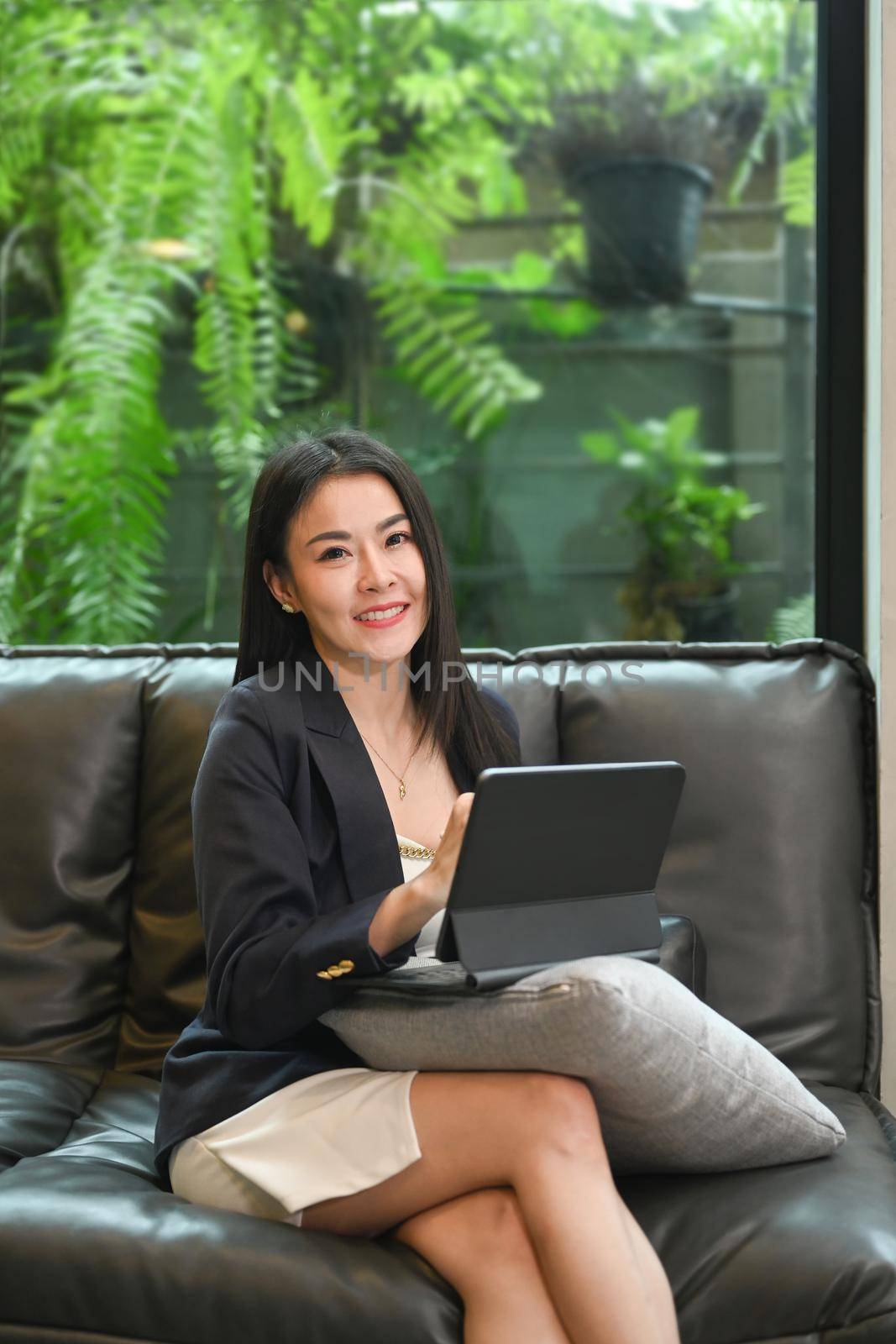 Attractive female entrepreneur sitting on couch in her office and using digital tablet.