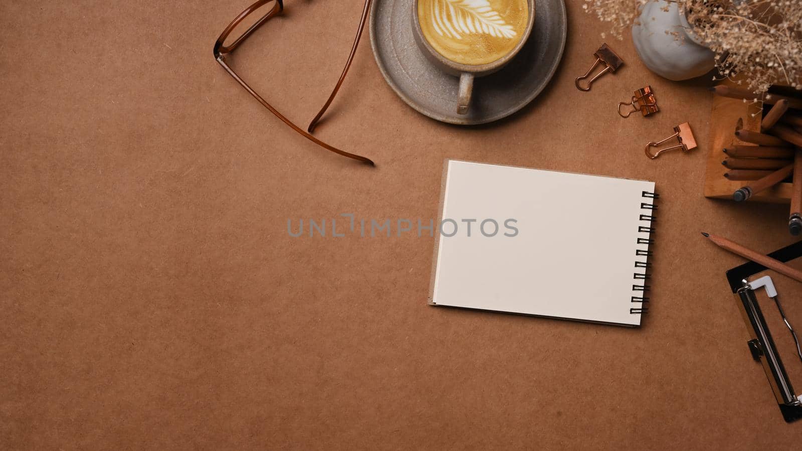 Top view notebook, coffee cup and glasses on brown background. by prathanchorruangsak