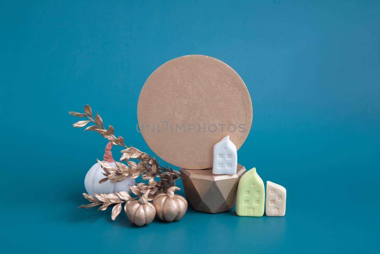 Still life of gold and white pumpkins, acorns and miniature houses on a turquoise background. Minimalistic autumn concept with copy space