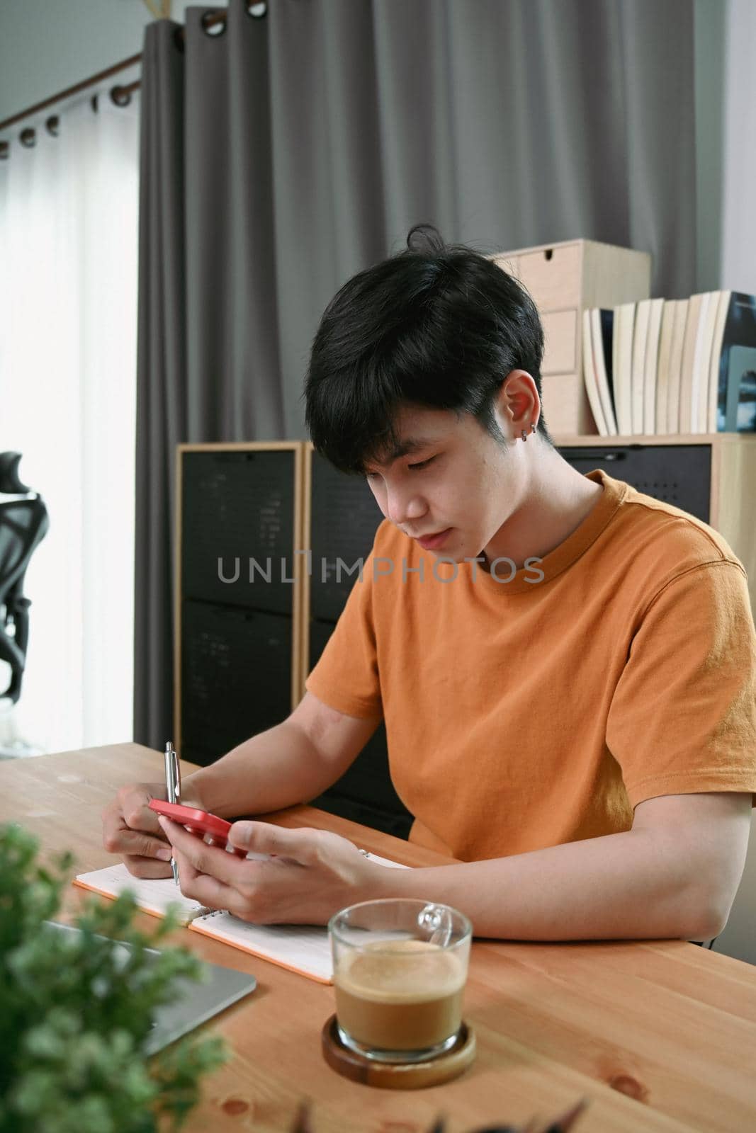 Young asian man using smart phone while sitting in home office.