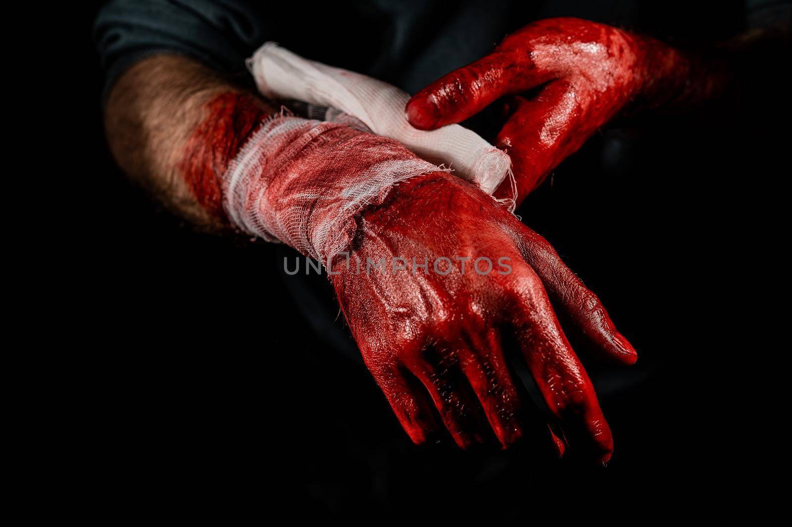 A man covered in blood bandages his hands