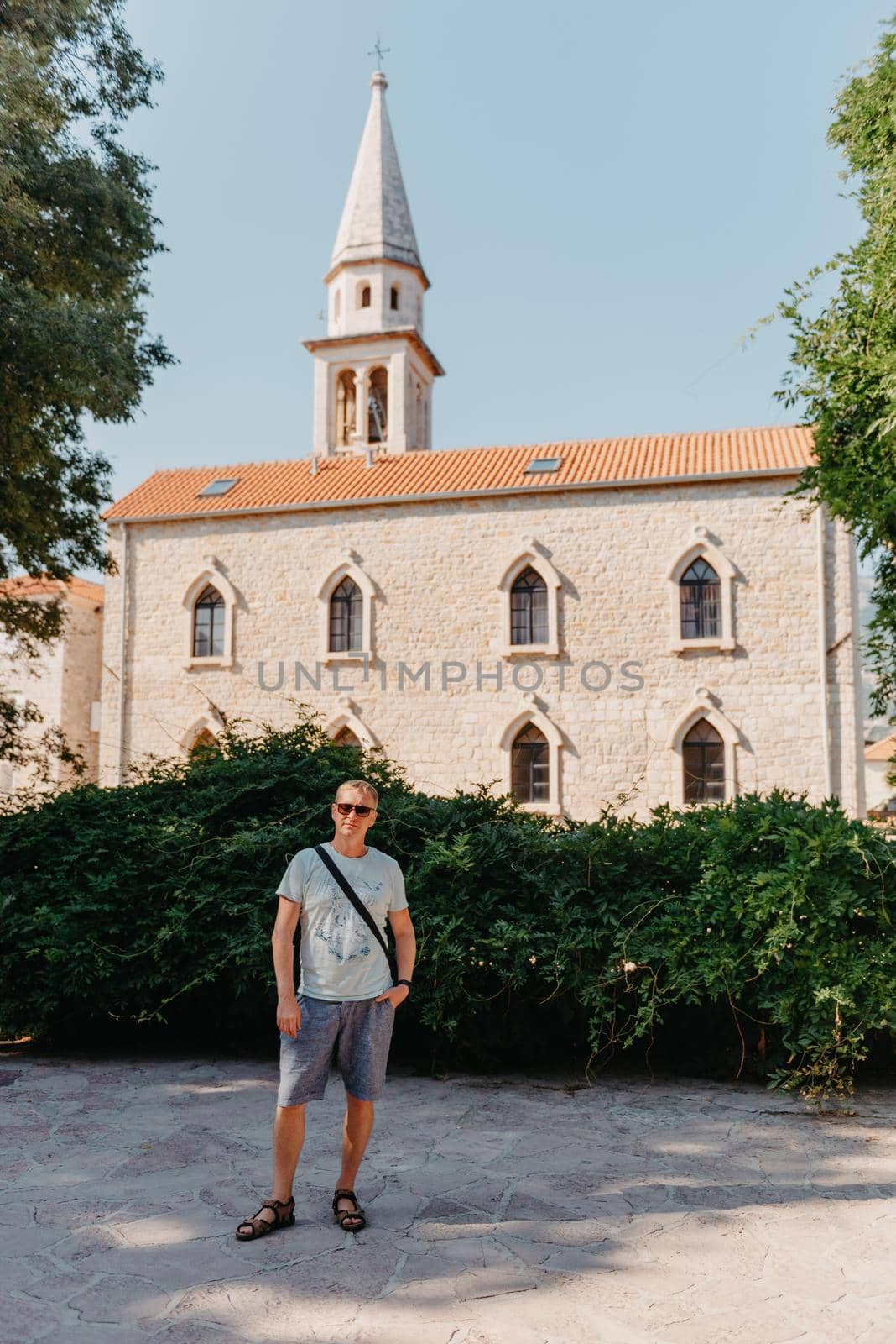 A handsome young man standing and smiling happily in the background of urban buildings. Forty years old caucasian tourist man outdoor near old city buildings - summer holiday. by Andrii_Ko