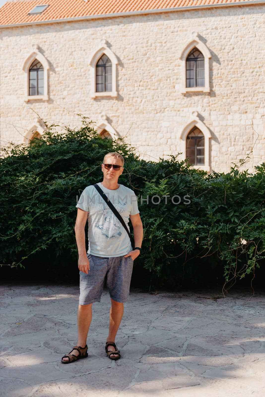 A handsome young man standing and smiling happily in the background of urban buildings. Forty years old caucasian tourist man outdoor near old city buildings - summer holiday. by Andrii_Ko