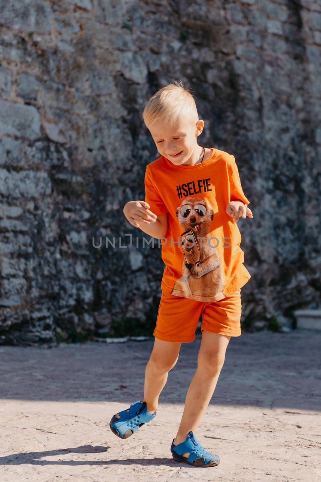 Kid's outdoor activity. Smile toddler boy wearing a orange shorts Jumping, running and having fun in a backyard on a sunny hot summer day. Full length of energetic little boy in stylish casual outfit jumping outdoor