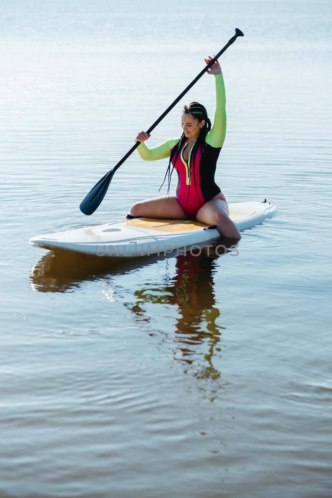 Young Woman with Dreadlocks in Swimwear Sitting on the Sup Board, Female Paddleboarding on Lake at Sunrise
