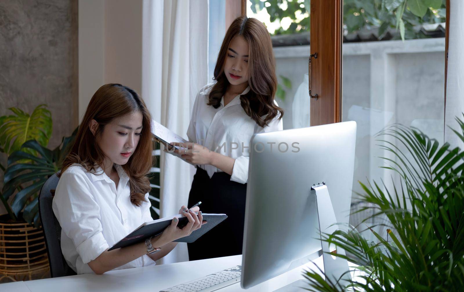 Two young beautiful asian business woman in the conversation, exchanging ideas at work..