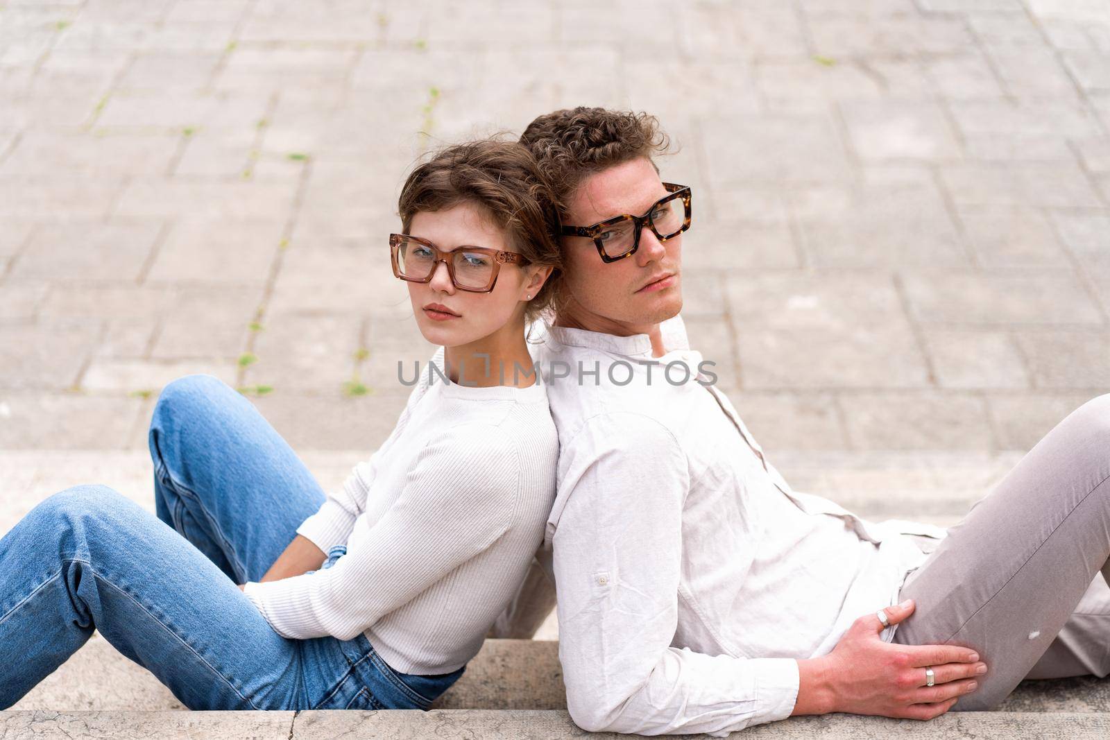 Two attractive students man and woman wearing stylish glasses sitting floor by andreonegin