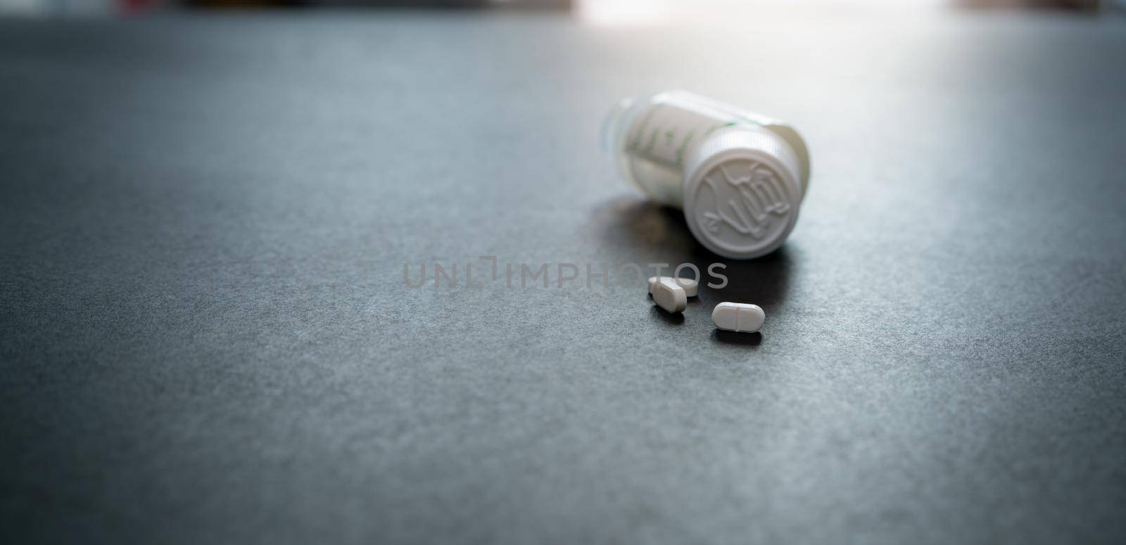 White tablets pills and blur child-resistant pill bottle on black table. Prescription drugs. Pharmaceutical industry. Medical care. Medication for cure illness. Pharmacy product. Small white tablets.