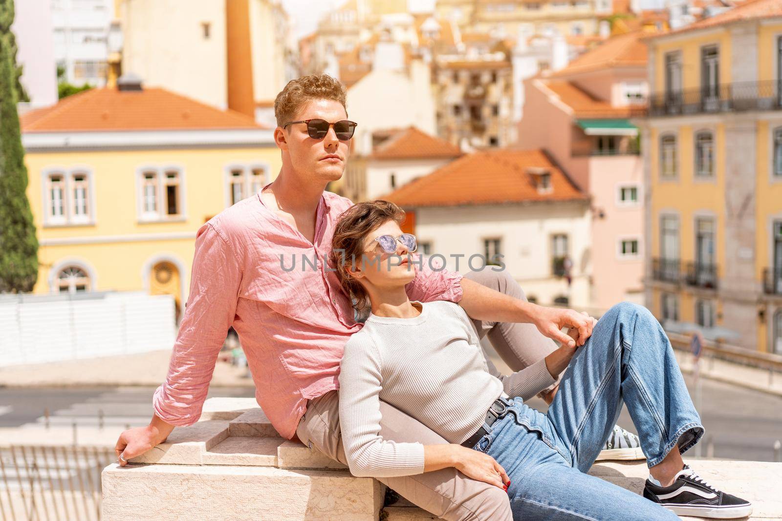 Young beautiful hipster couple in sunglasses in love sitting stairs on old city street by andreonegin
