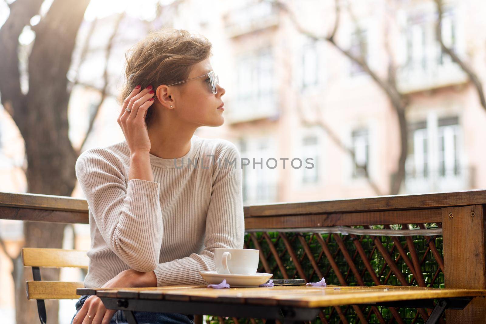 Portrait of thoughtful young woman sitting at table with coffee and looking away, pensive charming young woman posing at free time and waiting friend or boyfriend.