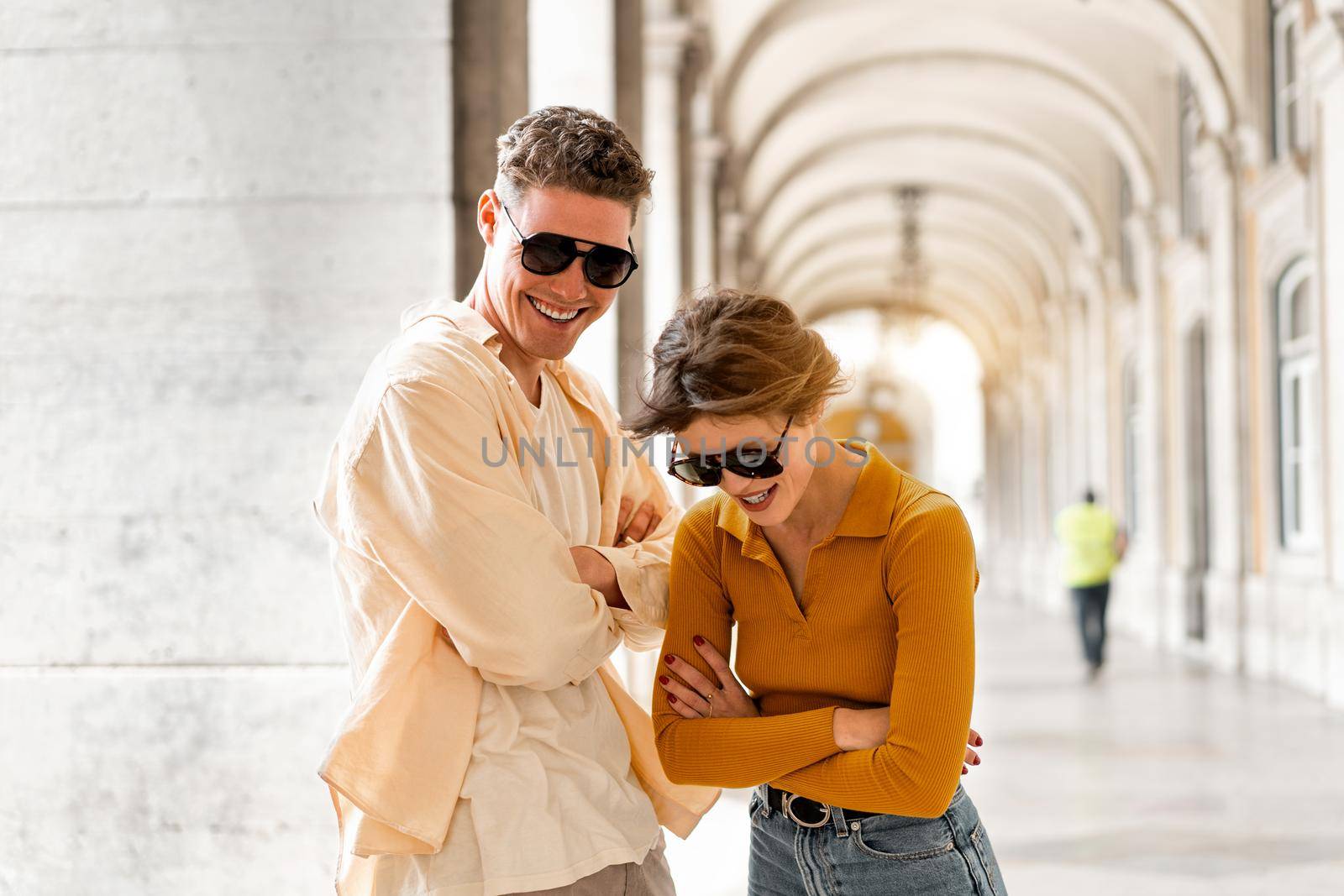 Young beautiful hipster couple in sunglasses in love walking on old city street by andreonegin