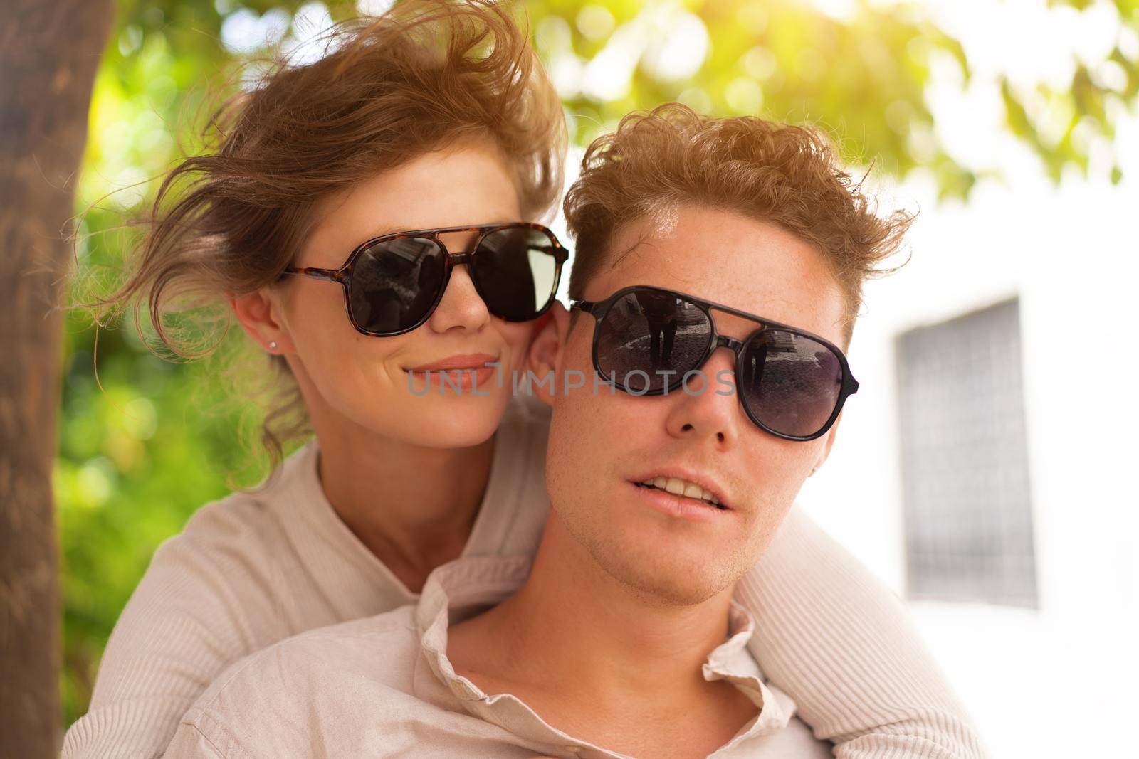 Smiling beautiful woman and her handsome boyfriend. Woman embrace summer day. Happy cheerful couple in sunglasses walking old city park. Couple posing on the street near green tree Headshot portrait