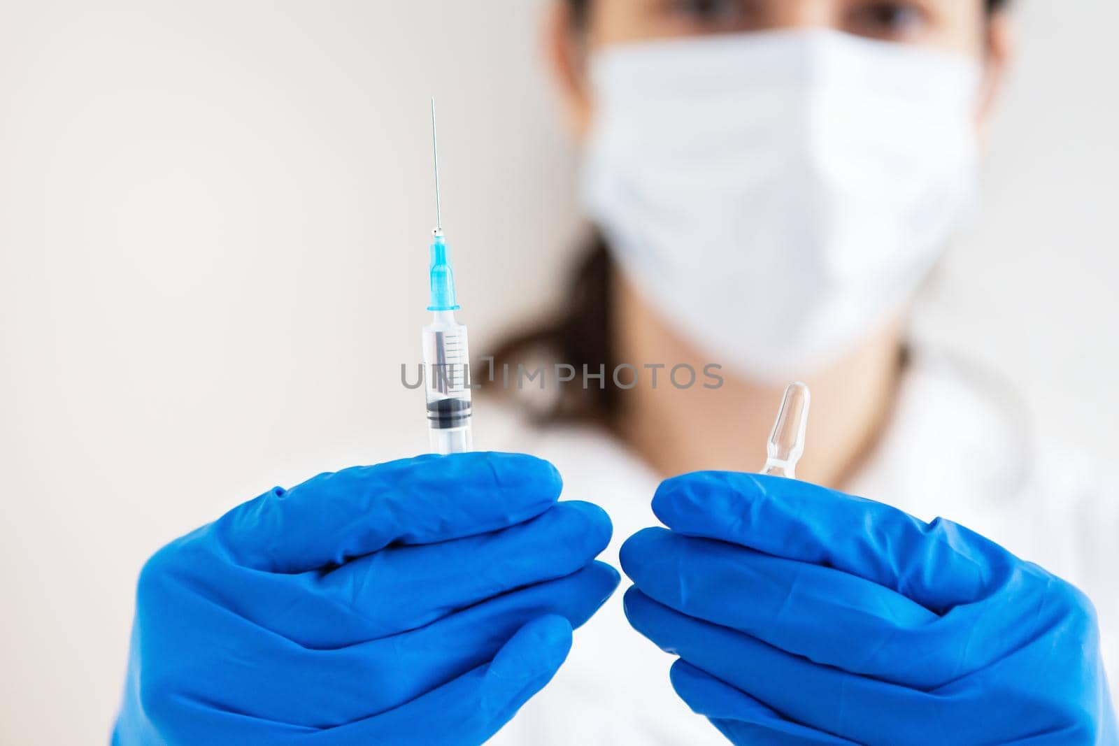 A young doctor with a syringe and a vaccine in his hands. Doctor indoors makes vaccination. A woman in a medical office. Vaccination against influenza and viruses. by sfinks