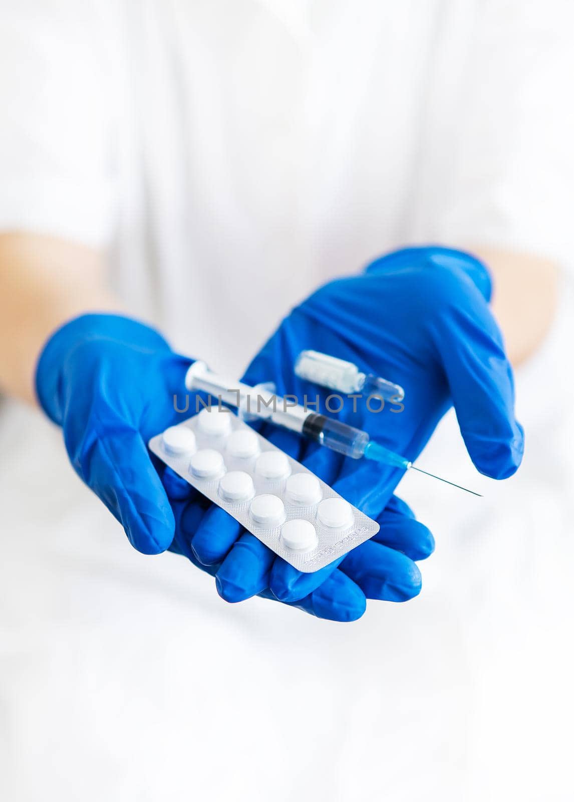 A young doctor holds a vaccine, syringe and pills in latex blue gloves. Doctor indoors makes vaccination. A woman in a medical office. Vaccination against influenza and viruses