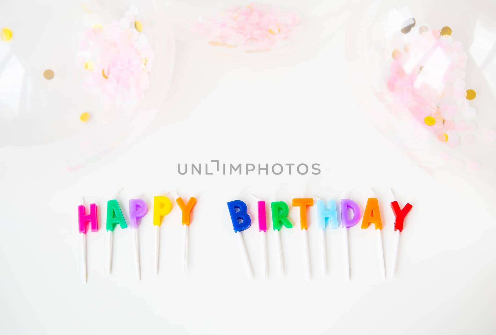 Colorful candles with the inscription Happy Birthday isolated on a white background along with confetti. Holiday and surprise concept