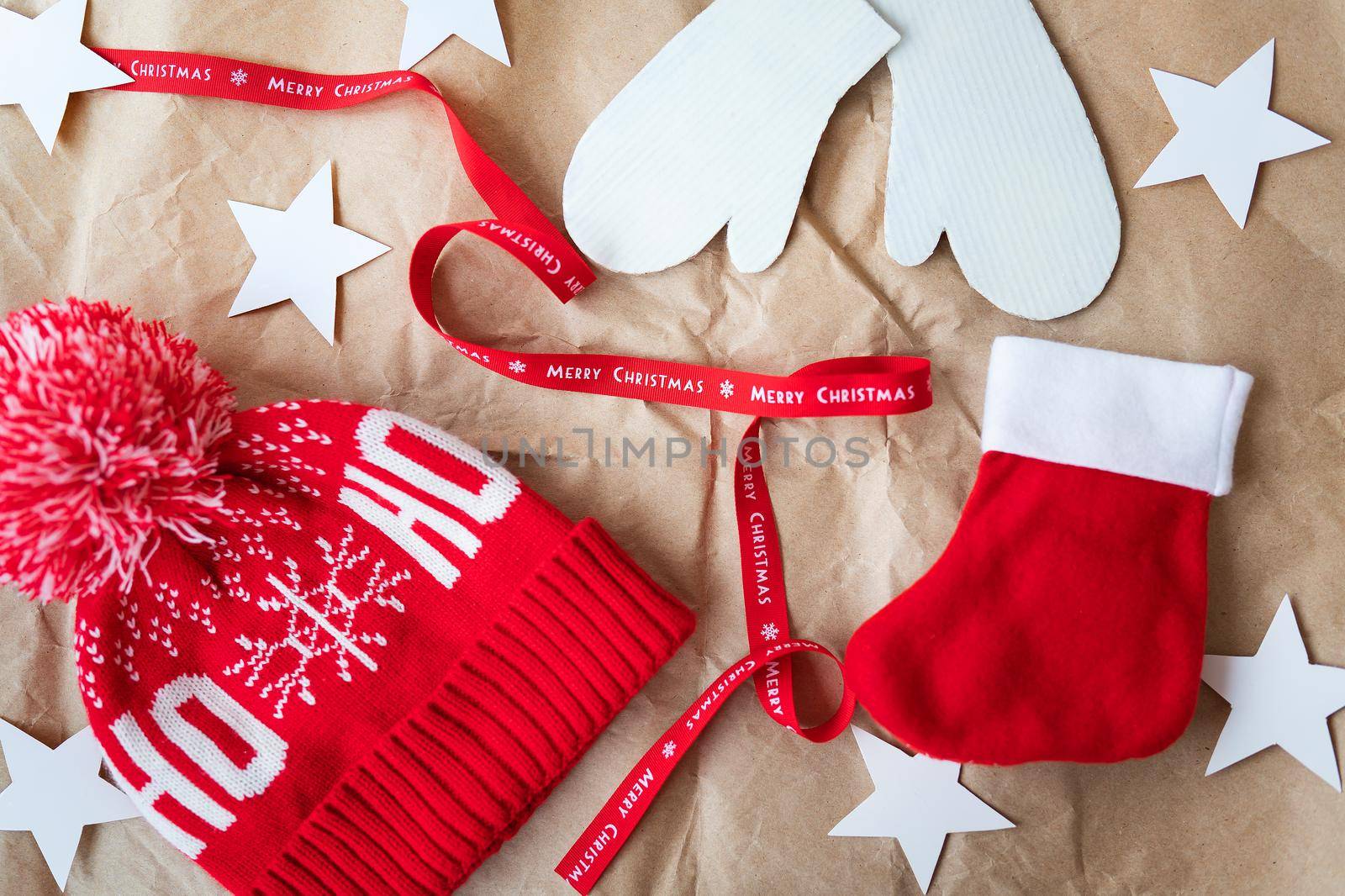 Red ribbon with the inscription Merry Christmas along with a red cap, mittens, red sock spread out on craft paper. Christmas celebration concept on December 25th