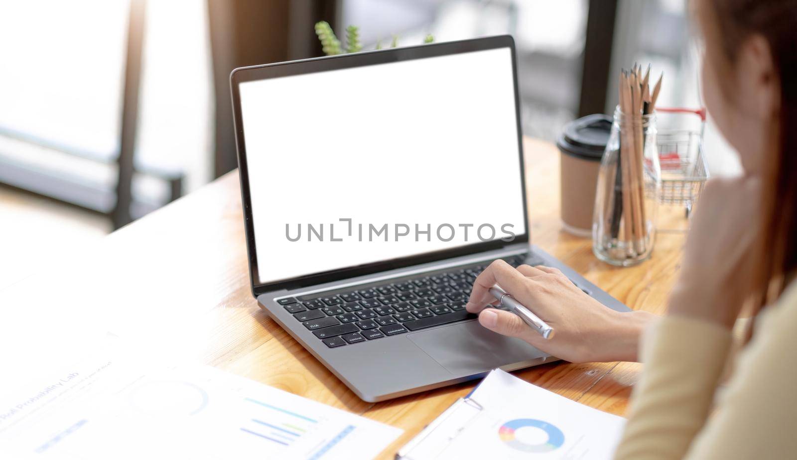 Mockup image of a woman using and typing on laptop computer with blank white desktop screen on wooden table by wichayada