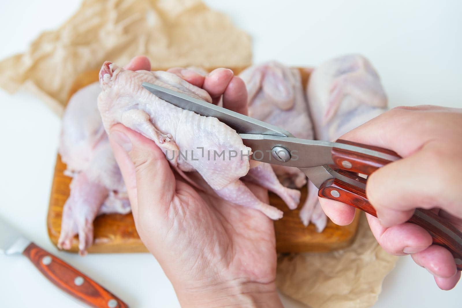 Raw quails lie on a wooden board. A man uses scissors to cut diet lean meat