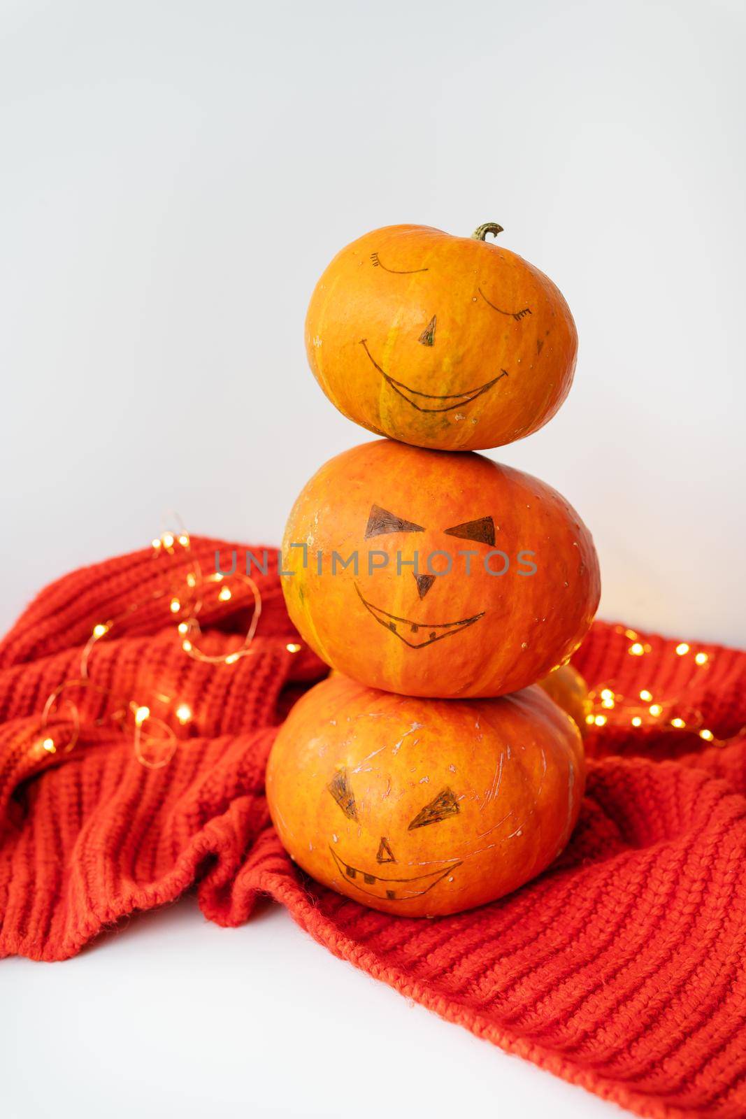 Three pumpkins with a painted face on a red sweater. The concept of the holiday on October 31, Halloween. Nice bokeh in the background