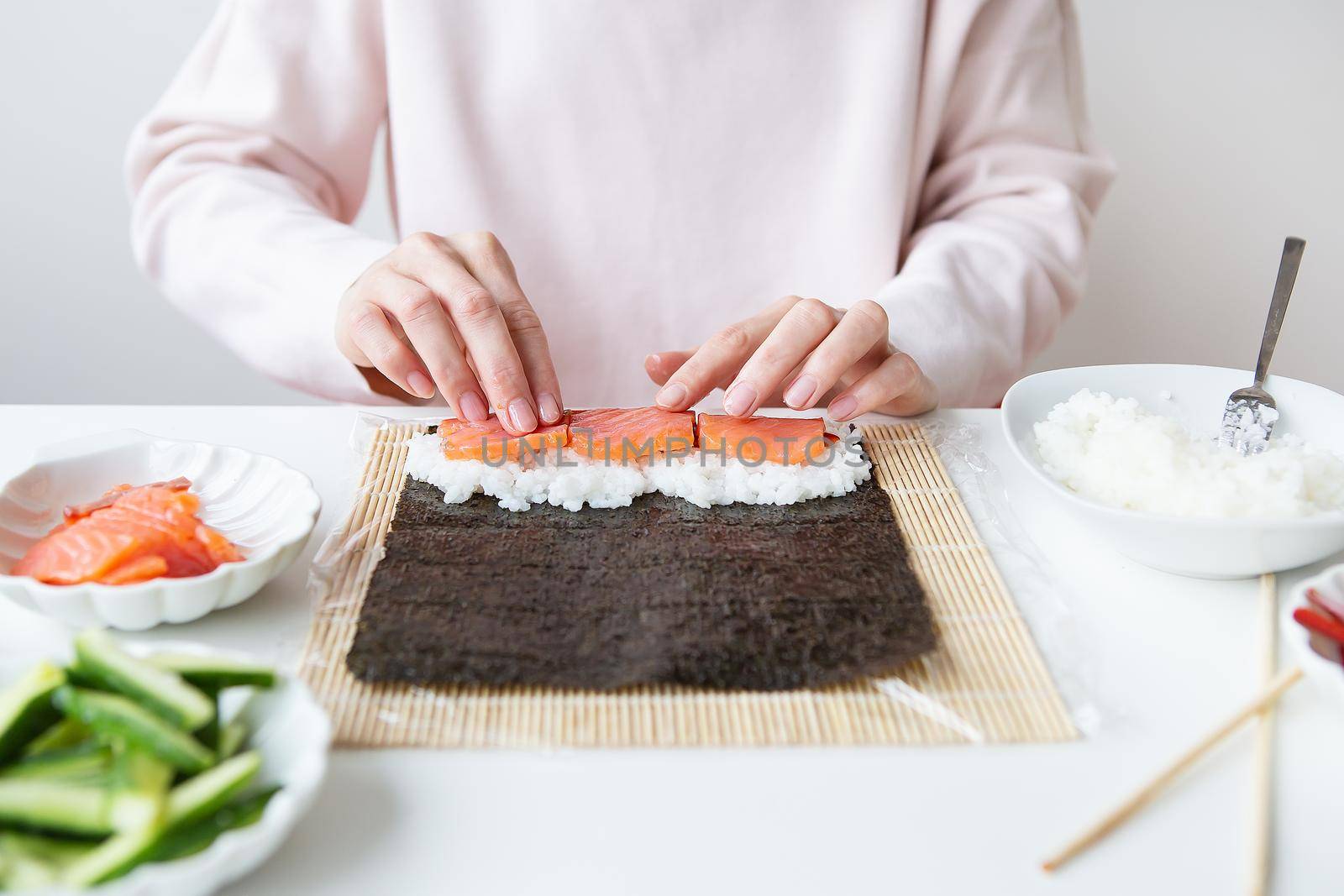 Sushi preparation process, the girl makes sushi with different flavors - fresh salmon, caviar, avocado, cucumber, ginger, rice. by sfinks