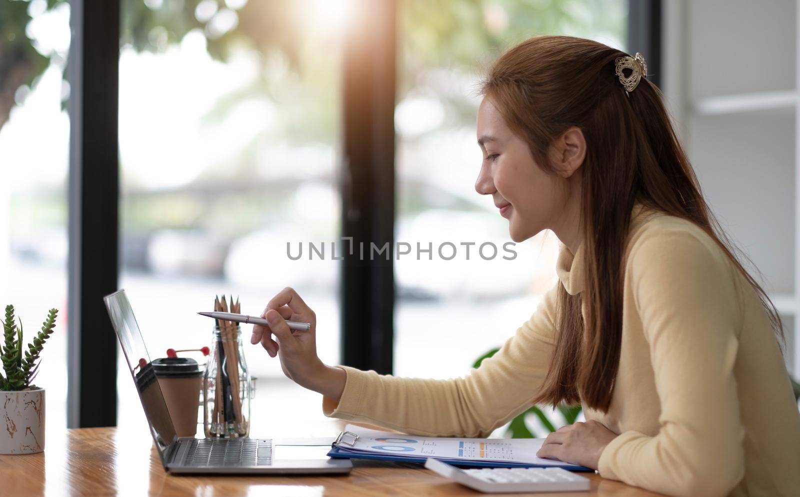 Business woman pen pointing turnover with graph chart report on laptop computer for analysis data by wichayada