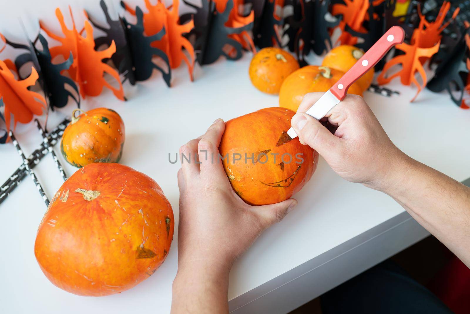 Halloween October 31st. A man cuts the face of a pumpkin with a knife. View from above