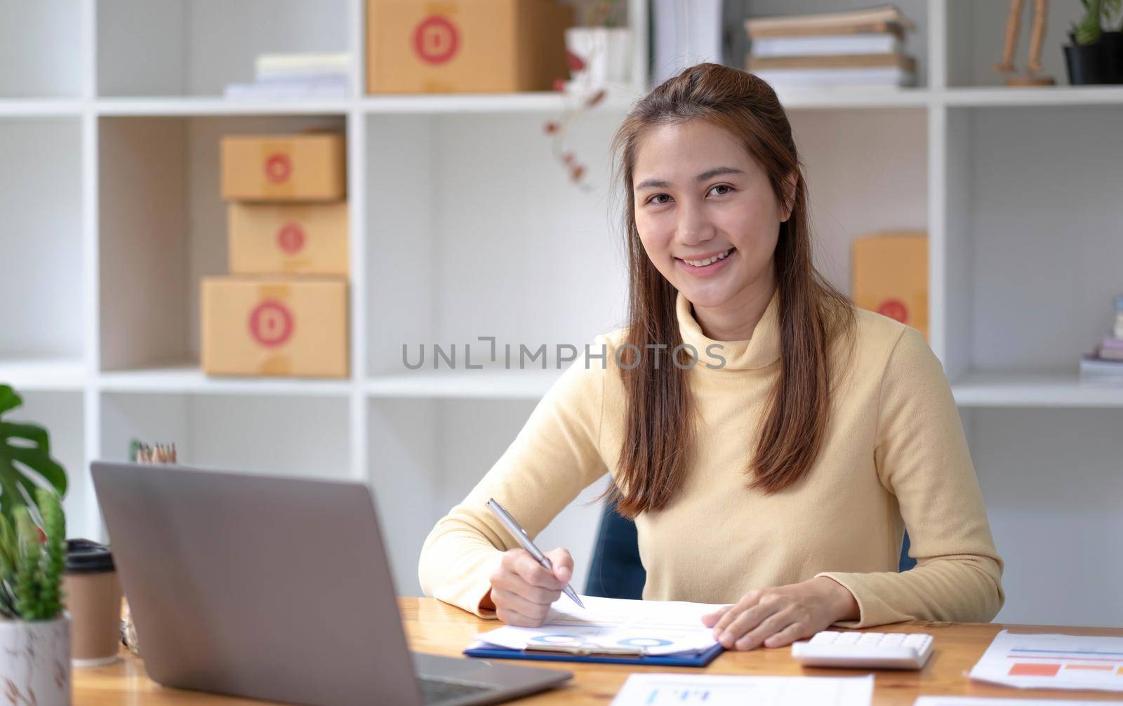 Small business entrepreneur SME freelance,Portrait of young asian woman working at home office,online marketing packaging delivery box,e-commerce business concept. by wichayada