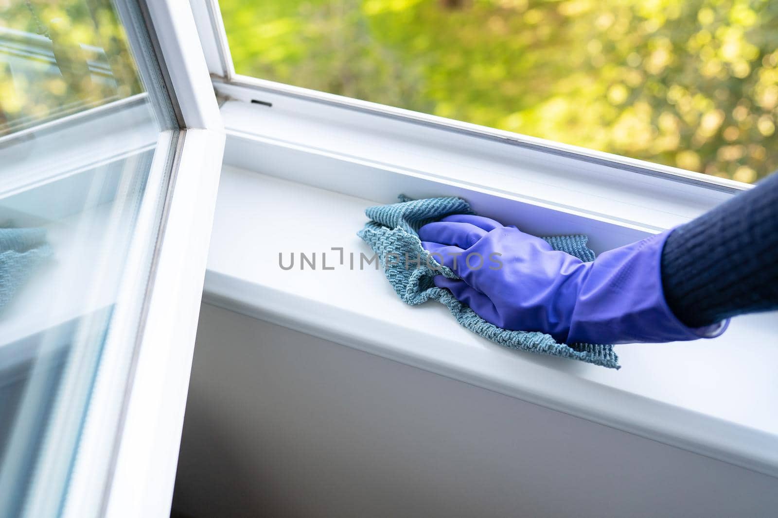 Cleaning and cleaning concept. A young girl in purple gloves wipes the dust on the windowsill with a rag