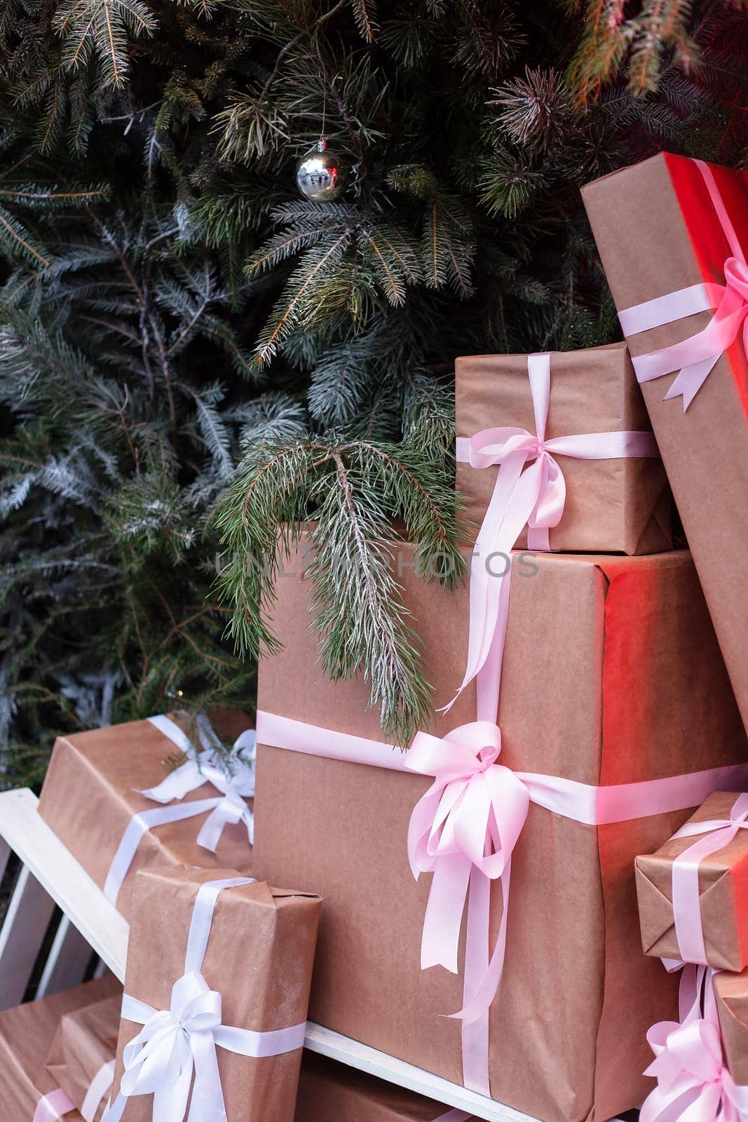 Craft gift boxes on the street near a wall made of a Christmas tree and fir. Christmas and New Year concept. December 25