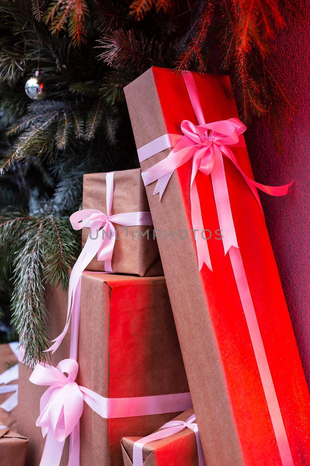 Craft gift boxes on the street near a wall made of a Christmas tree and fir. red neon shines on boxes.Christmas and new year concept. December 25