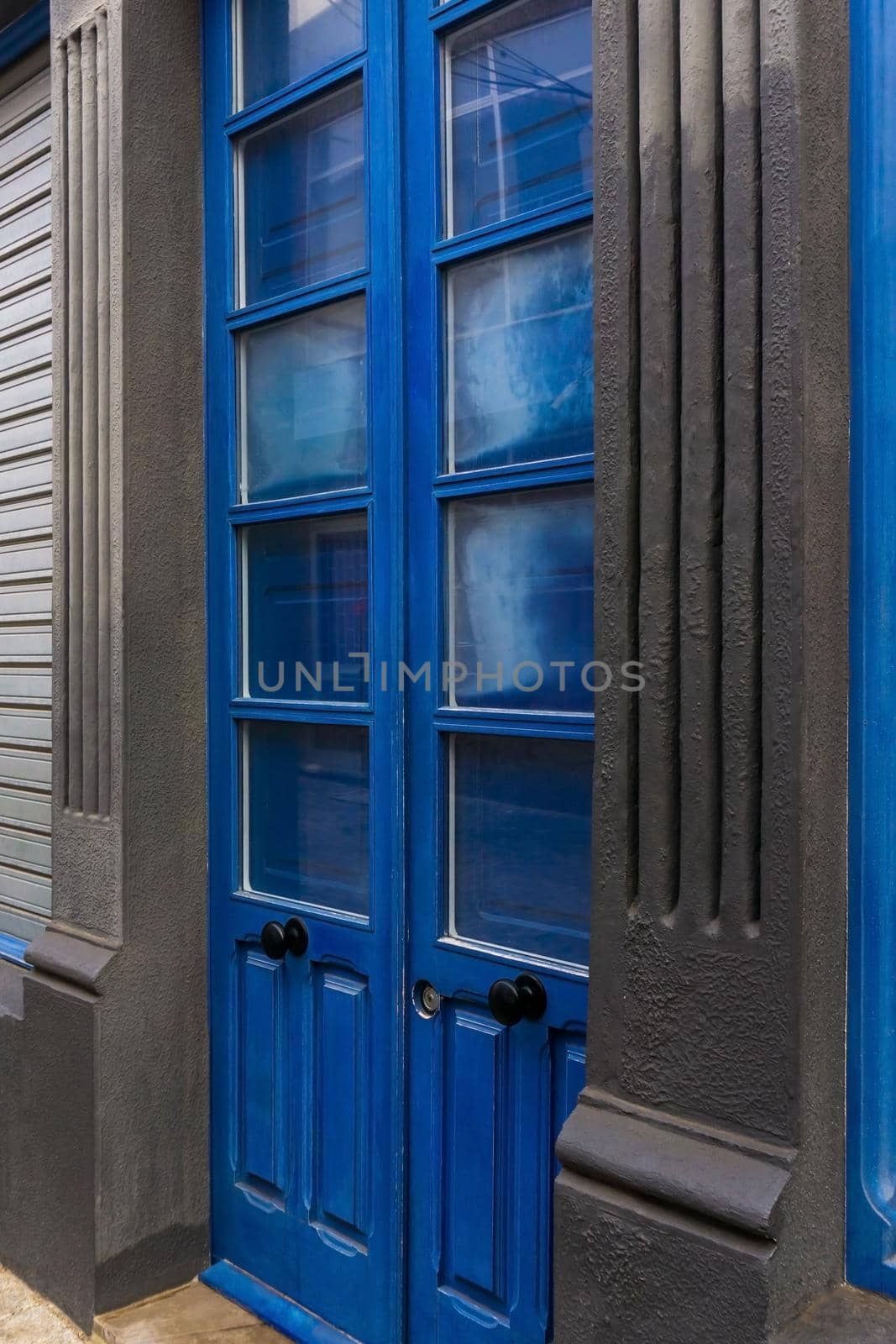 Blue wooden double door with glass windows closed shutters against the background of gray walls