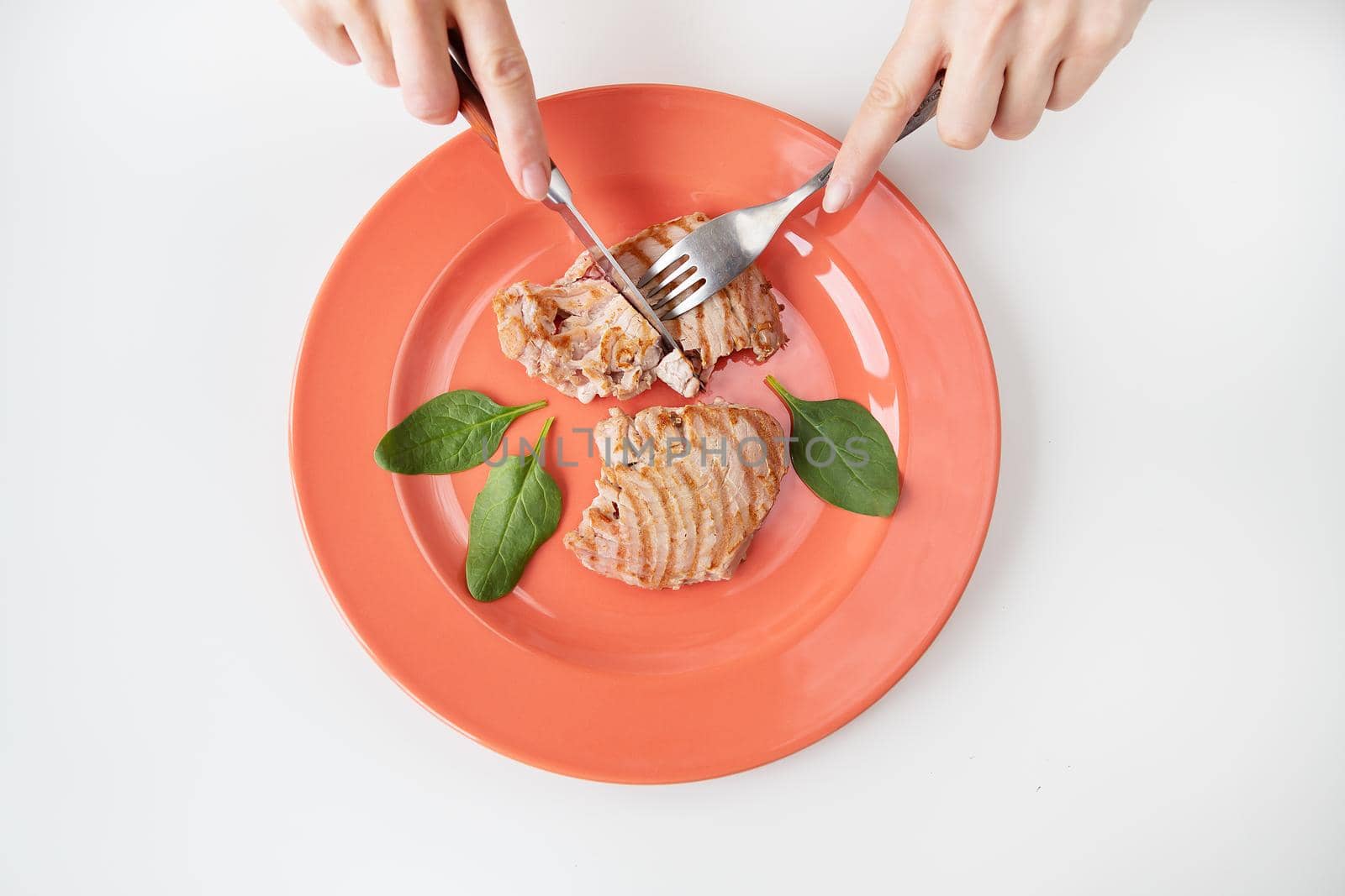 Close-up shot of a juicy delicious grilled tuna steak on a bright coral plate. Delicious and healthy and wholesome food, proper nutrition. The girl is holding a fork and knife