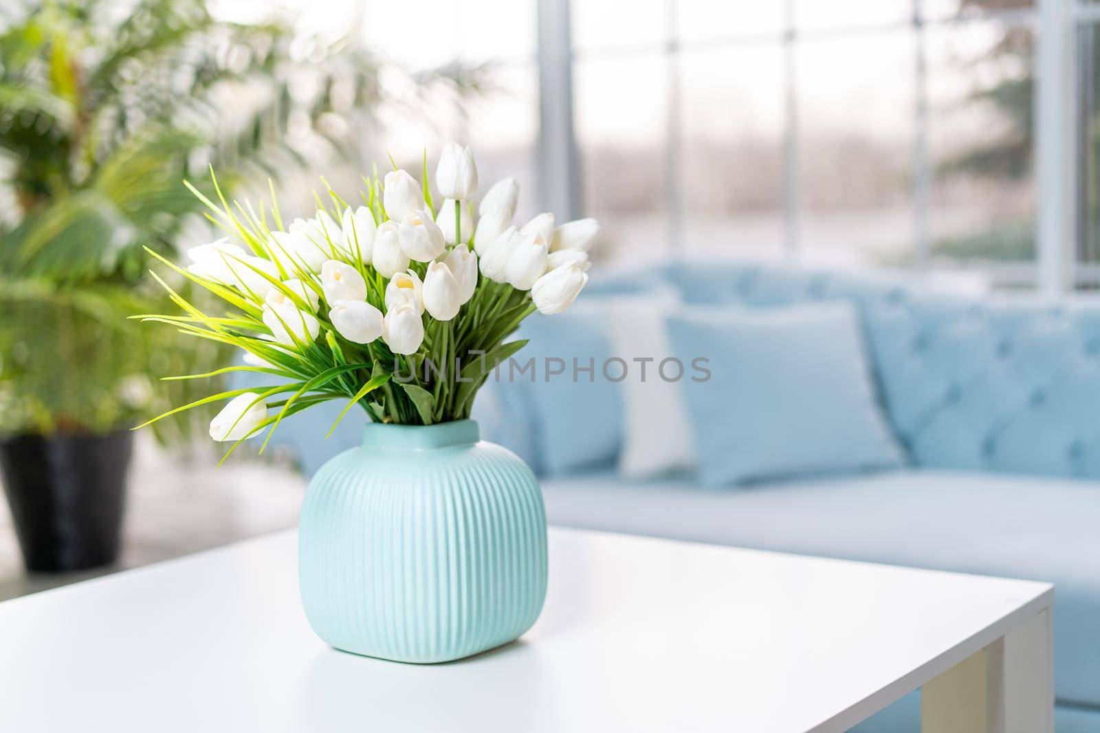 Luxury house interior. ELegant living room Modern Interior design. White Living Room Tulip flowers standing vase on coffee table With big panoramic window on background