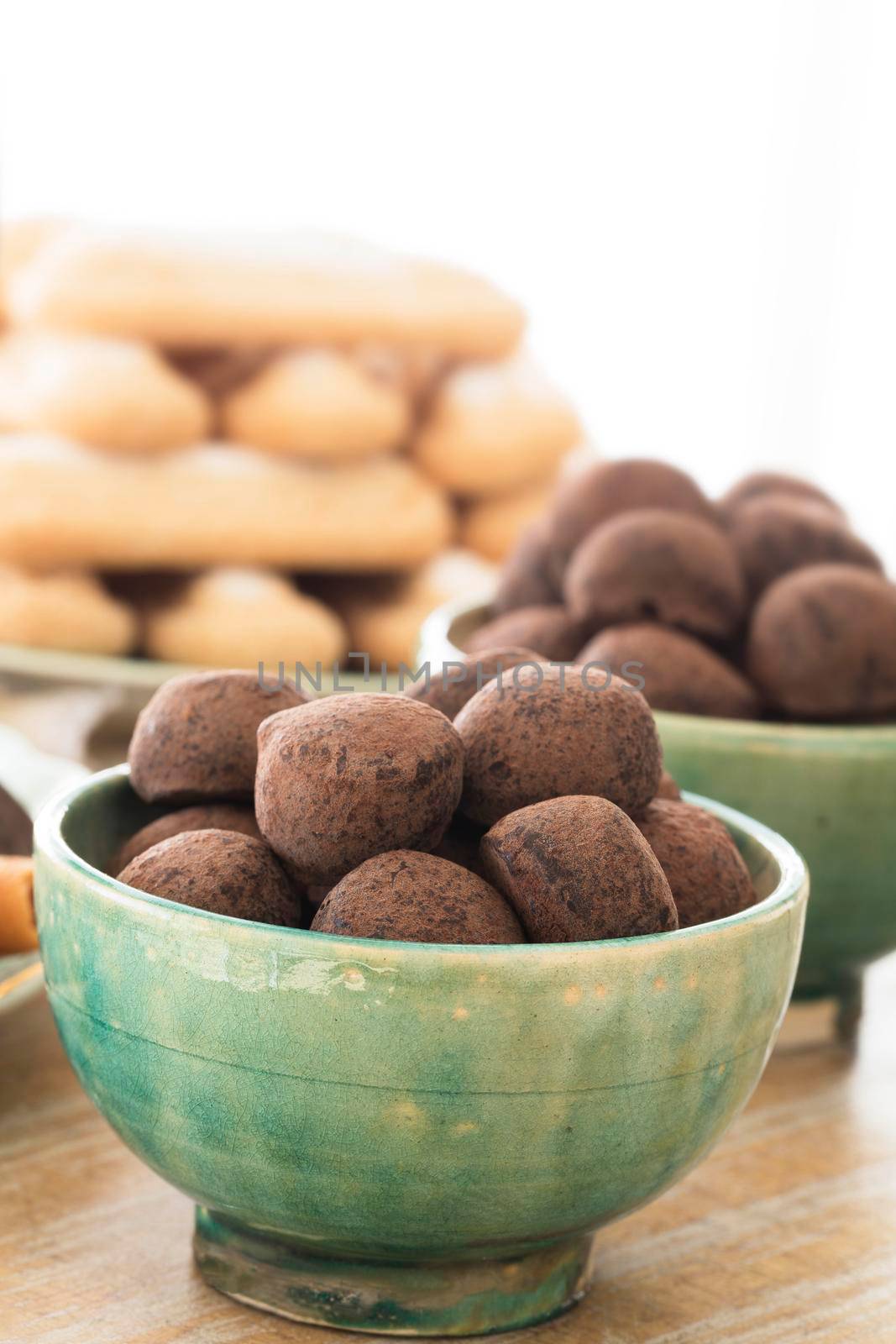 Close up of chocolate truffles in green bowl with ladyfingers in background and copy space