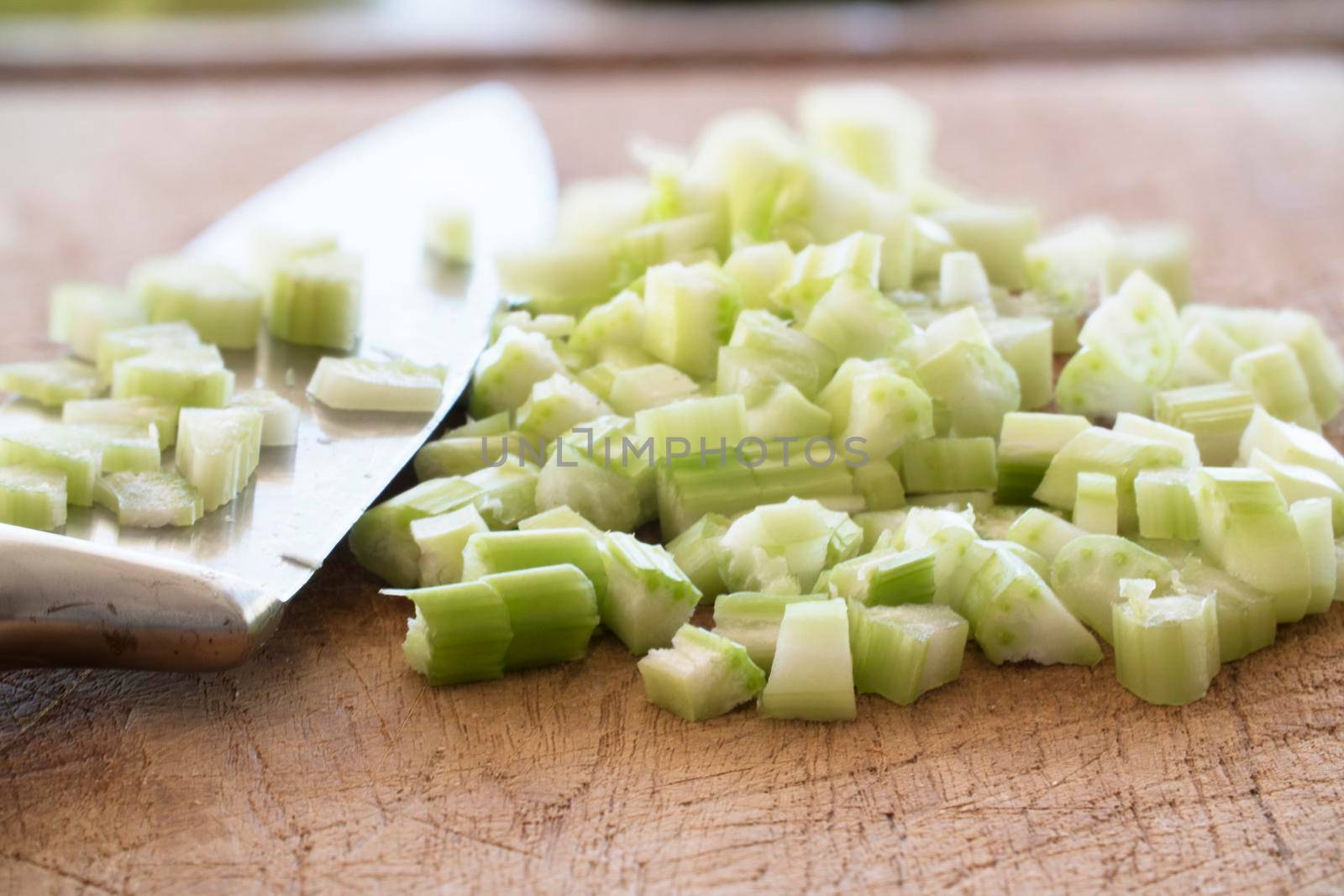 Close up of chopped celery with knife on cutting board.