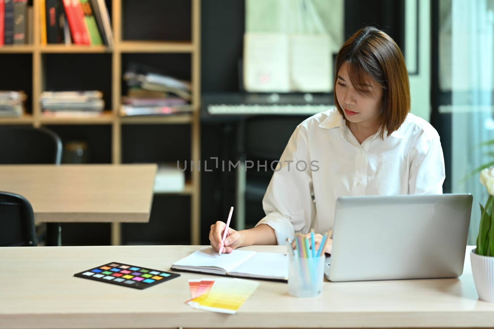 Focused asian woman working on creative project at contemporary workplace by prathanchorruangsak