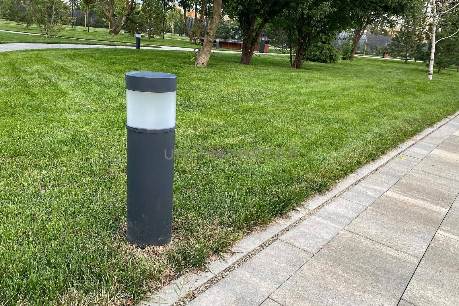 marble path of square tiles, lantern mounted on a green lawn in the park, daylight. copy space.