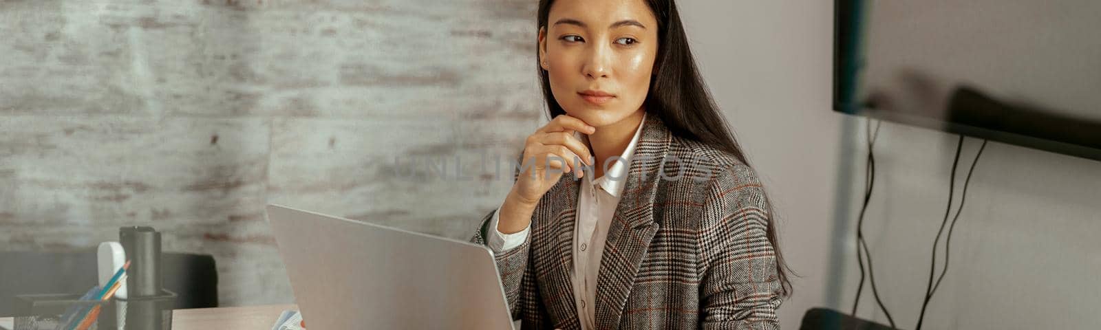 Pretty asian business woman working laptop sitting in modern office and looking away by Yaroslav_astakhov