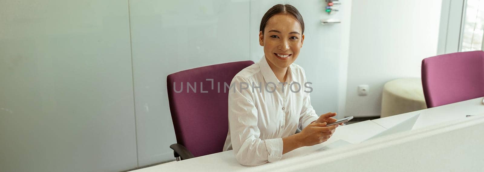 Smiling asian business woman sitting in meeting room and holding phone. High quality photo