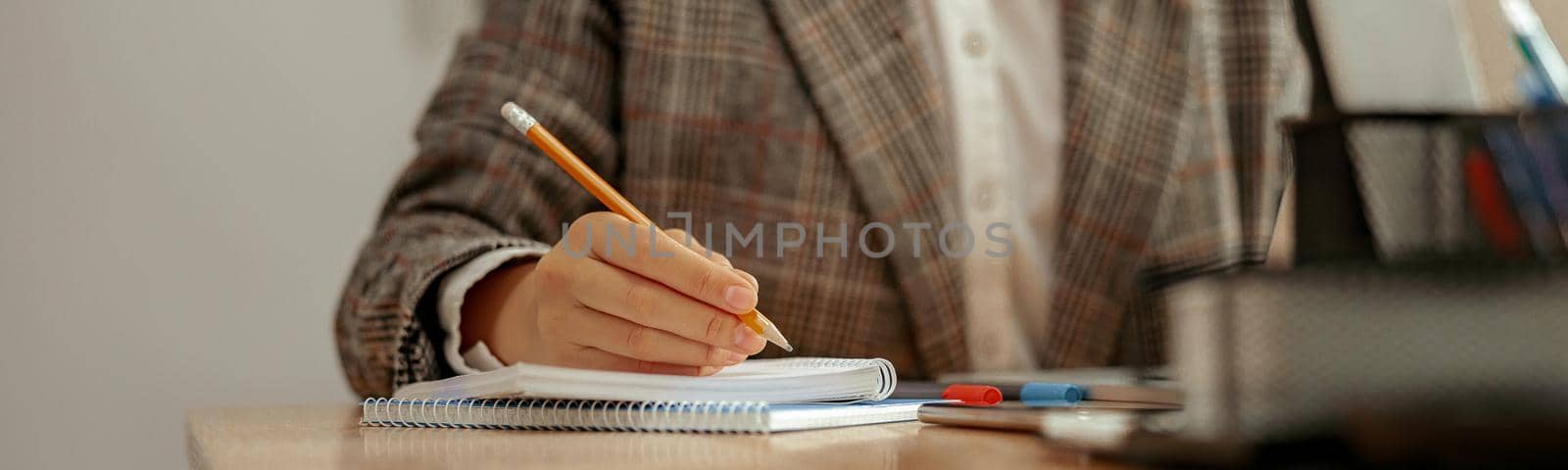 Close-up of unrecognizable business woman taking notes in notebook while sitting at workplace